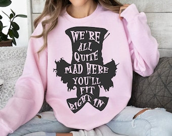 Può includere: Felpa rosa con una silhouette nera del cappello del Cappellaio Matto e il testo "We're all quite mad here you'll fit right in".
