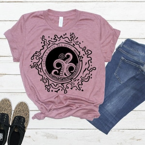 May include: A mauve t-shirt with a black graphic of an octopus with the text "Ursula's Deep Sea Repo" and "You can't get something for nothing".