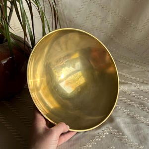 May include: A large, round, polished brass bowl. The bowl is empty and has a reflective surface.