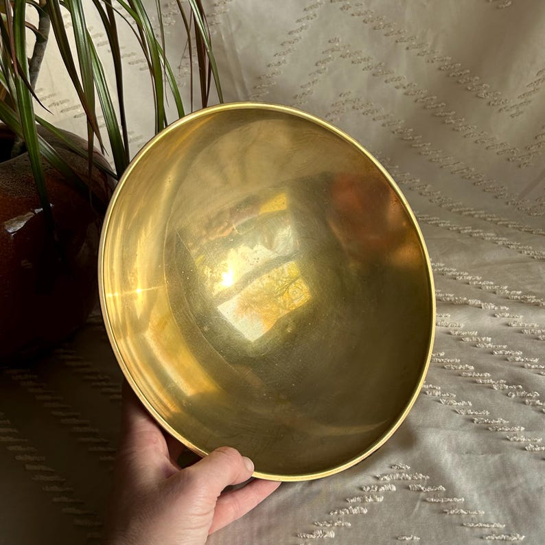 May include: A large, round, polished brass bowl. The bowl is empty and has a reflective surface.