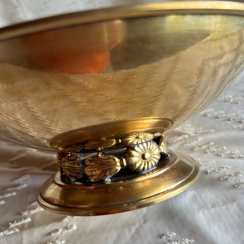 May include: A gold metal bowl with a decorative base. The base features a ring of gold floral designs.