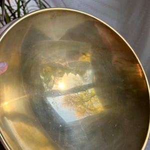 May include: A large, round, brass bowl with a reflective surface. The bowl is empty and appears to be made of polished brass.