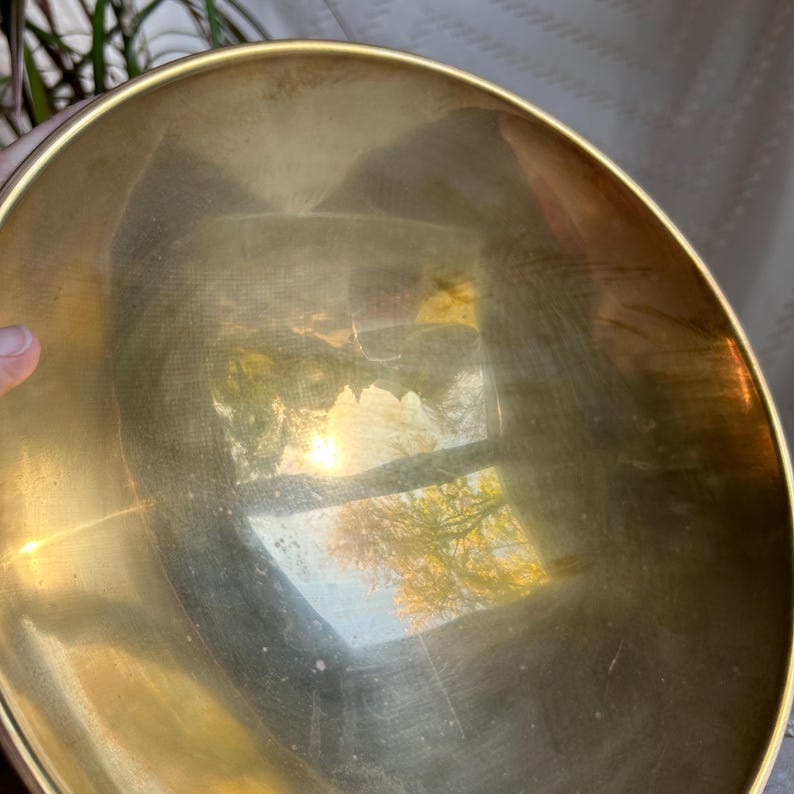 May include: A large, round, brass bowl with a reflective surface. The bowl is empty and appears to be made of polished brass.