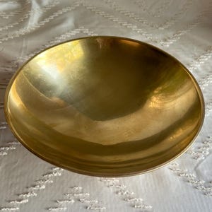 May include: A large, round, brass bowl with a smooth, shiny surface.