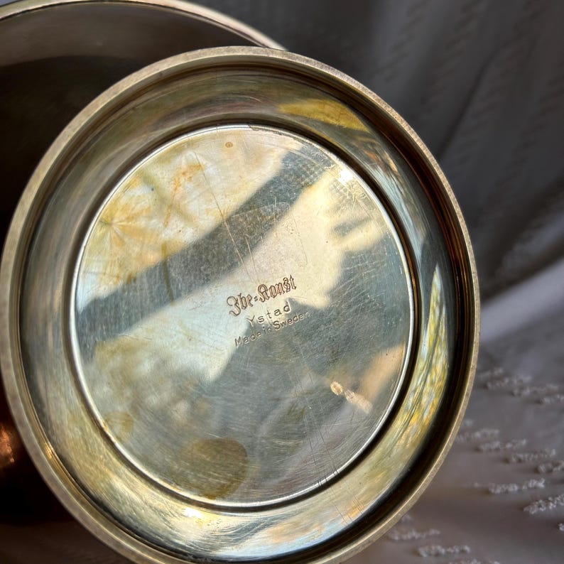 May include: The bottom of a silver bowl with the inscription "3br-Ronsh Ystad Made in Sweden".