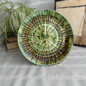 May include: A green and brown ceramic plate with a swirling, tie-dye pattern. The plate is on a white stand.