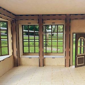 Könnte beinhalten: Ein Miniatur-Holzraum mit einer Tür und Fenstern. Die Fenster haben ein Gittermuster, und die Tür hat einen gewölbten oberen Teil. Der Innenraum ist hell, mit einem gefliesten Boden und Blick auf grünes Gras und Bäume draußen.