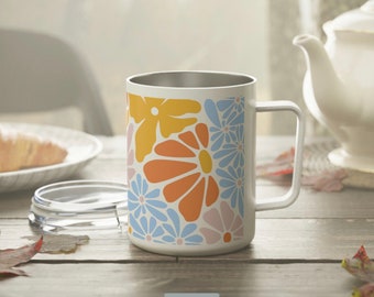 May include: A white stainless steel travel mug with a floral design featuring blue, orange, yellow, and pink flowers. The mug has a lid and a handle.