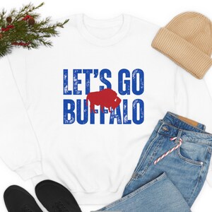 May include: White sweatshirt with blue and red text that says "Let's Go Buffalo" with a red buffalo silhouette.