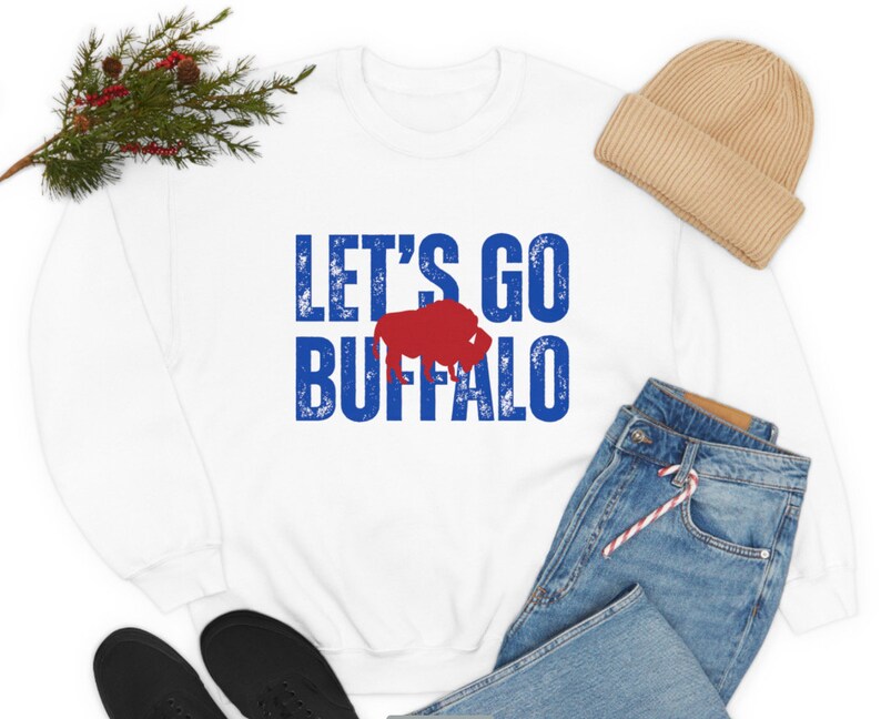 May include: White sweatshirt with blue and red text that says "Let's Go Buffalo" with a red buffalo silhouette.