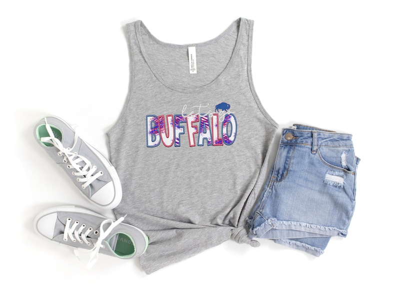 May include: A gray tank top with the text "Let's go Buffalo" in red, white, and blue with a buffalo silhouette. The tank top is paired with denim shorts and gray sneakers.