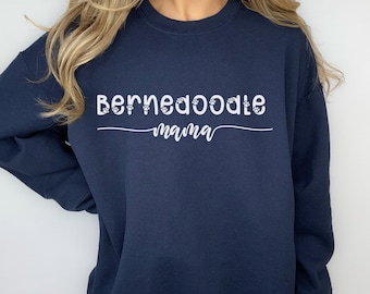 Puede incluir: Una sudadera azul marino con el texto "Bernedoodle mama" en letras blancas. Las letras están decoradas con huellas de patas.