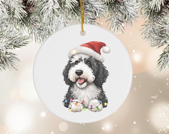 Op de afbeelding: Een witte keramische kerstbal met een zwart-witte hond die een rode kerstmanmuts draagt en kleurrijke kerstverlichting vasthoudt.
