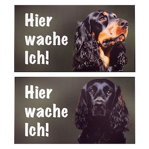 Könnte beinhalten: Zwei rechteckige Schilder mit dunkelgrünem Hintergrund. Das obere Schild zeigt einen Hund mit schwarzem und braunem Fell und den Text "Hier wache Ich!" in Weiß. Das untere Schild zeigt einen schwarzen Hund mit demselben Text.