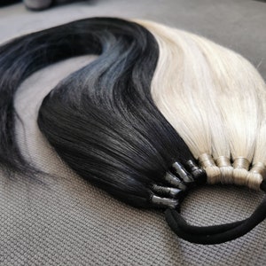 May include: A black and blonde ombre hair extension with a black elastic band. The hair is tied together with black and brown clips.