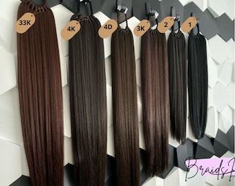 Può includere: Sette extensioni di capelli umani di diverse tonalità di marrone e nero, ciascuna legata con un elastico nero. Le extensioni sono etichettate con numeri e lettere, tra cui 33K, 4K, 4D, 3K, 2 e 1.