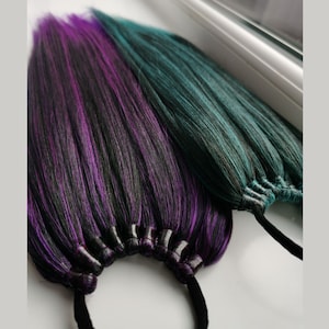 Può includere: Due pacchetti di extension per capelli sintetici, uno con sfumature di nero, viola e turchese, e l'altro con sfumature di nero e turchese. Entrambi i pacchetti sono legati insieme con elastici neri.