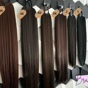 Peut inclure: Sept extensions de cheveux de différentes nuances de brun et de noir, chacune avec un élastique brun et une étiquette avec un numéro et la lettre K. Les étiquettes indiquent 33K, 4K, 4D, 3K, 2 et 1.