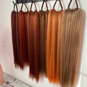 May include: A set of eight hair extensions in various shades of red, orange, and brown, hanging from a black metal rack.
