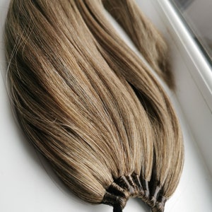 May include: A long, brown and blonde hair extension with a black elastic band. The hair is tied together with multiple black bands.