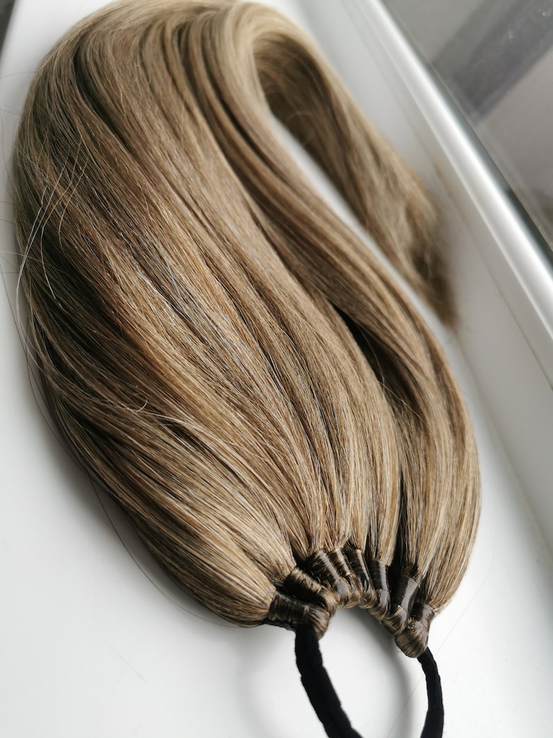 May include: A long, brown and blonde hair extension with a black elastic band. The hair is tied together with multiple black bands.
