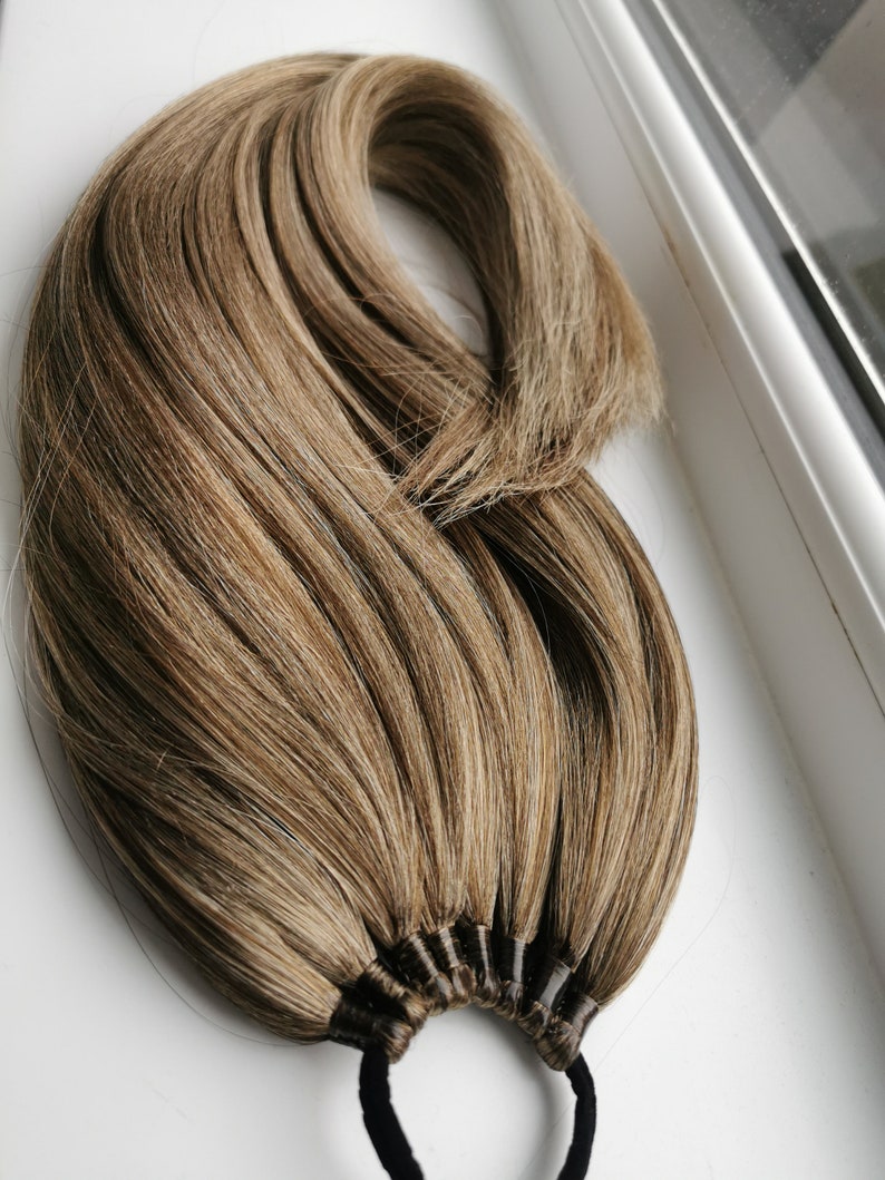 May include: A long, brown ponytail hair extension with a black elastic band. The hair is tied together with multiple black bands.