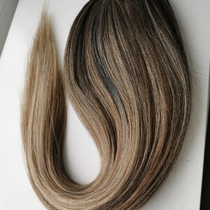 May include: A long, brown and blonde ombre ponytail hair extension with a brown elastic band.