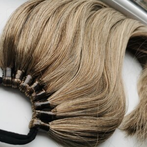 May include: A long, thick ponytail hair extension with a brown and blonde ombre color. The hair is tied with a black elastic band.