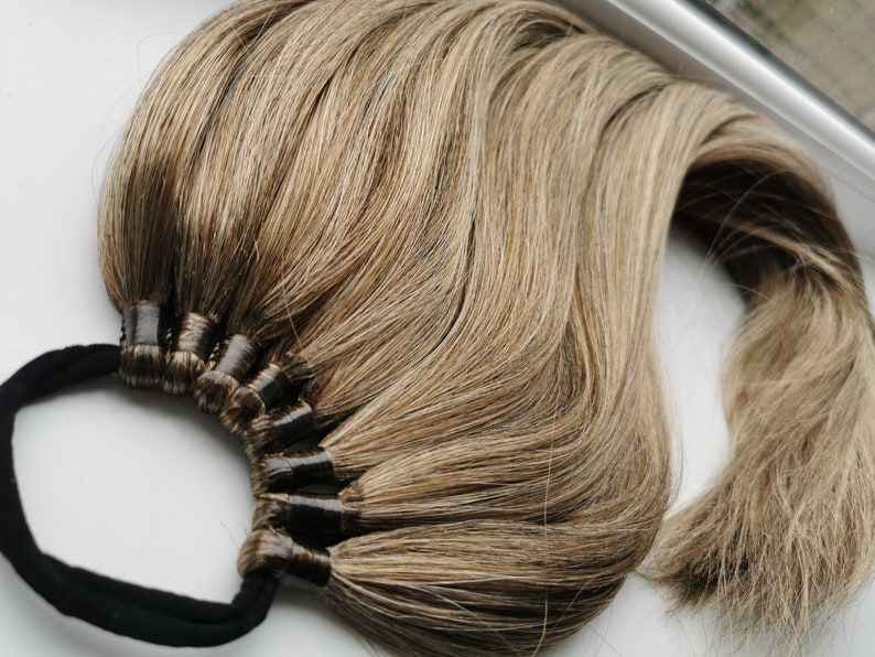 May include: A long, thick ponytail hair extension with a brown and blonde ombre color. The hair is tied with a black elastic band.