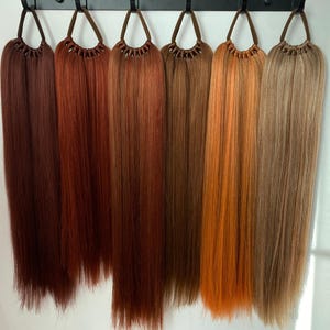 May include: Seven different shades of brown hair extensions hanging from hooks. The extensions are long and straight.