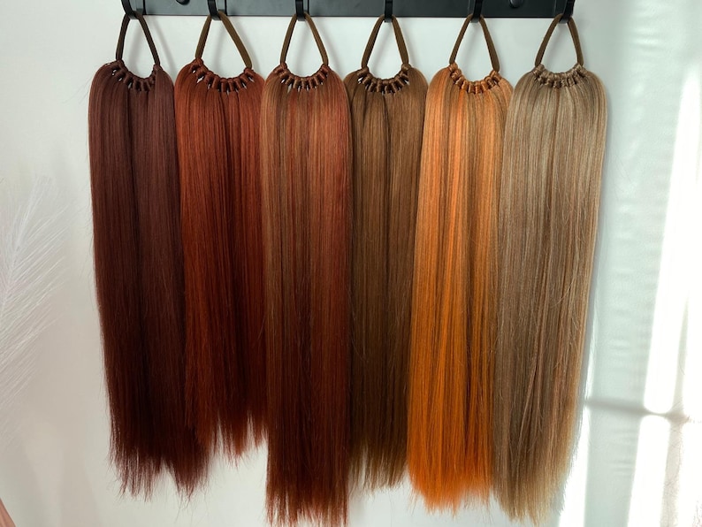 May include: Seven different shades of brown hair extensions hanging from hooks. The extensions are long and straight.