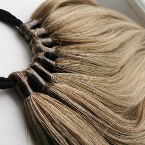 May include: A set of brown hair extensions with a black elastic band. The hair is long and straight, with a light brown and dark brown color.