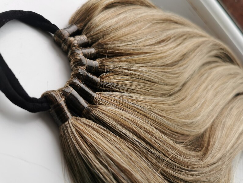 May include: A set of brown hair extensions with a black elastic band. The hair is long and straight, with a light brown and dark brown color.
