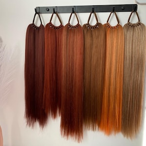 May include: Seven different shades of brown hair extensions hanging on a black rack. The hair extensions are long and straight.