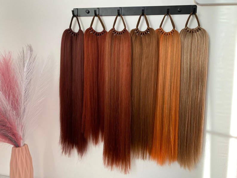 May include: Seven different shades of brown hair extensions hanging on a black rack. The hair extensions are long and straight.
