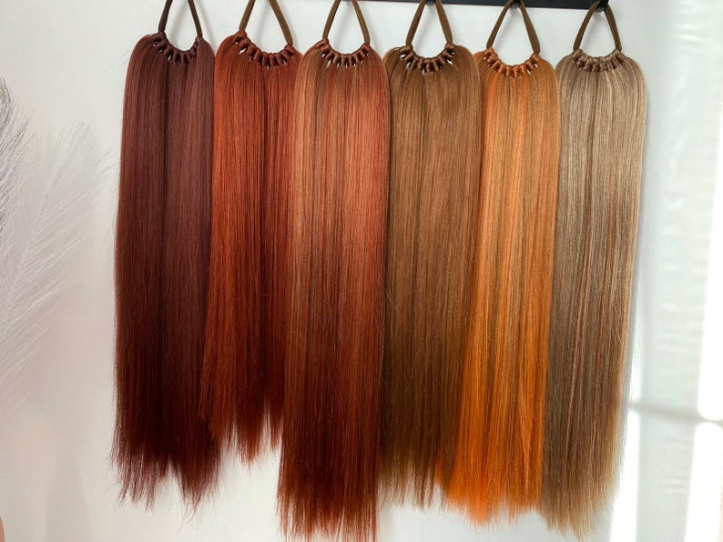 May include: Seven different shades of brown hair extensions, each with a brown elastic band at the top. The hair extensions are long and straight.