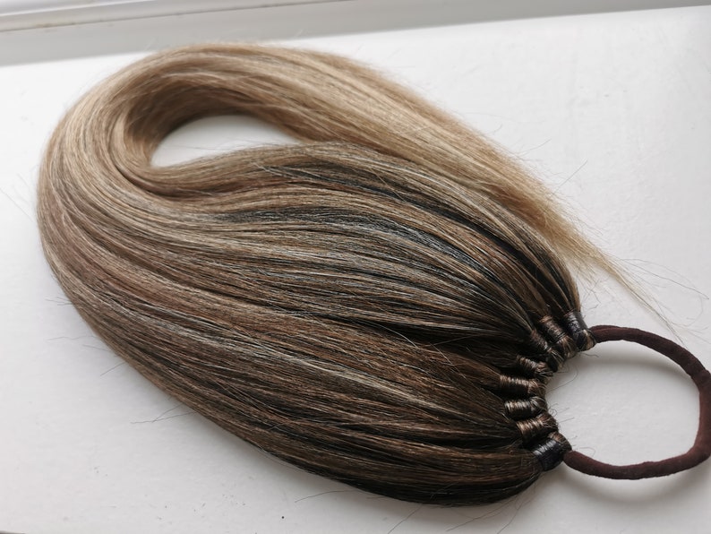 May include: A brown, blonde, and light blonde ponytail hair extension with a brown elastic band.