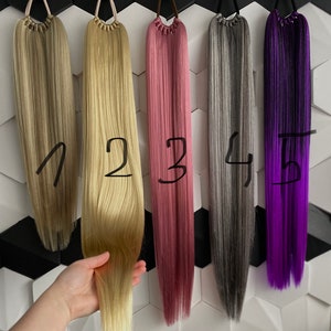 Op de afbeelding: Vijf verschillende gekleurde haarverlengingen met een clip aan de bovenkant. De verlengingen zijn genummerd van 1 tot en met 5. De kleuren zijn blond, lichtblond, roze, grijs en paars.