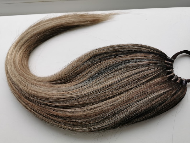 May include: A long, brown and blonde ombre hair extension with a brown elastic band.