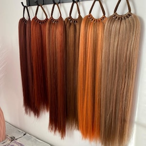 May include: A set of eight hair extensions in various shades of red, orange, and brown, hanging from a black metal rack.