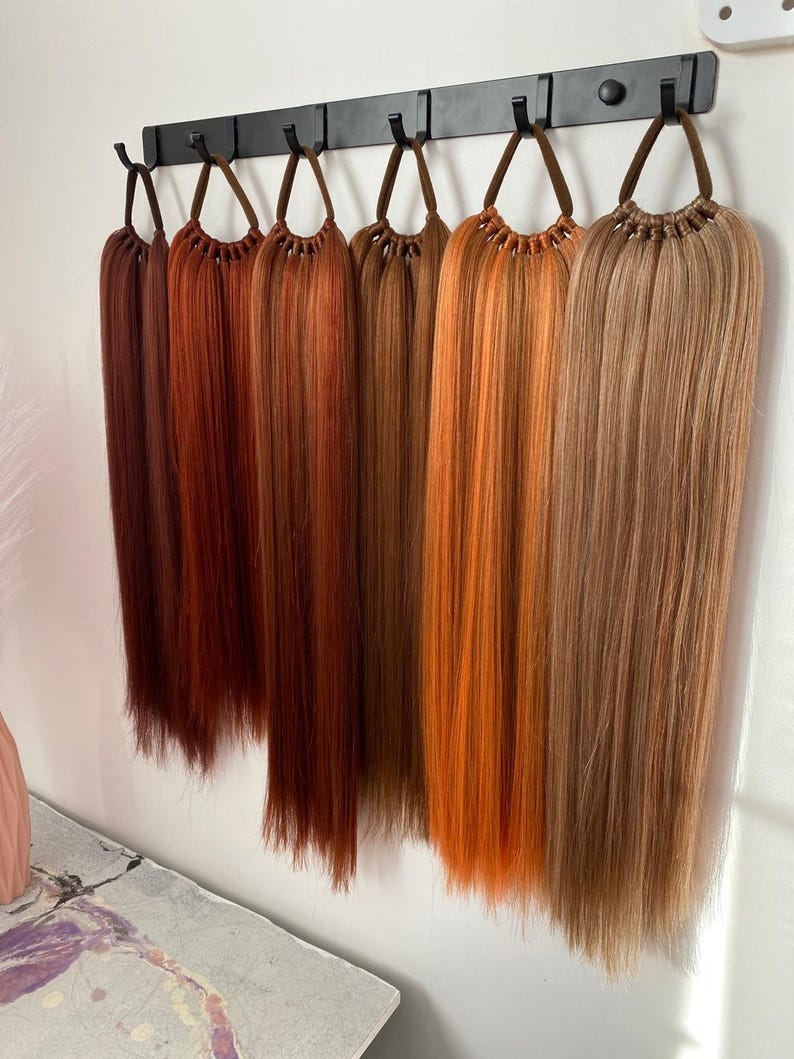 May include: A set of eight hair extensions in various shades of red, orange, and brown, hanging from a black metal rack.