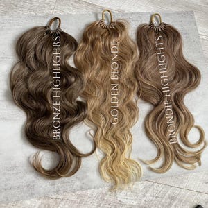 May include: Three wavy hair extensions in different shades. The colours are bronze highlights, golden blonde, and brondie highlights. Each bundle has a loop at the top for easy application. The text on the image indicates the hair colours.