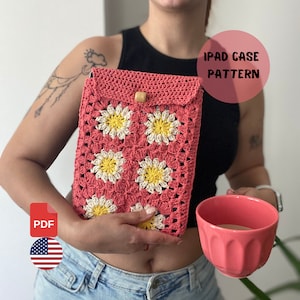May include: A crochet iPad case pattern featuring a pink and white daisy design. The pattern is available as a PDF download. The text "iPad Case Pattern" is visible in the image.