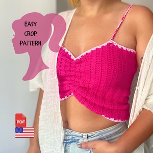 Op de afbeelding: Een roze gecrochete crop top met witte afwerking. De top heeft een gedraaid ontwerp en wordt gedragen door een persoon met een witte cardigan en een blauwe jeans. De tekst "EASY CROP PATTERN" is zichtbaar in de afbeelding.