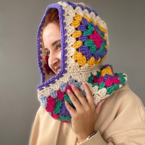 Puede incluir: Una colorida capucha de ganchillo con un patr&oacute;n de cuadrados de la abuela. La capucha presenta una base color crema con vibrantes cuadrados morados, amarillos, verdes y rosas. El borde de la capucha est&aacute; rematado con un borde morado, un accesorio acogedor y elegante.