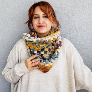 Puede incluir: Bufanda de cuello de ganchillo hecha a mano con un diseño de cuadrados de la abuela. La bufanda presenta una mezcla de colores cálidos, como amarillo mostaza, óxido, verde azulado y crema. La bufanda se lleva alrededor del cuello, ofreciendo un accesorio cómodo y elegante.