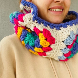 Puede incluir: Un cuello de ganchillo colorido con un patr&oacute;n de cuadrados de la abuela. El cuello presenta una mezcla de colores brillantes, incluyendo rosa, azul, amarillo, verde y crema. El cuello est&aacute; dise&ntilde;ado para ser usado alrededor del cuello y es un art&iacute;culo hecho a mano.