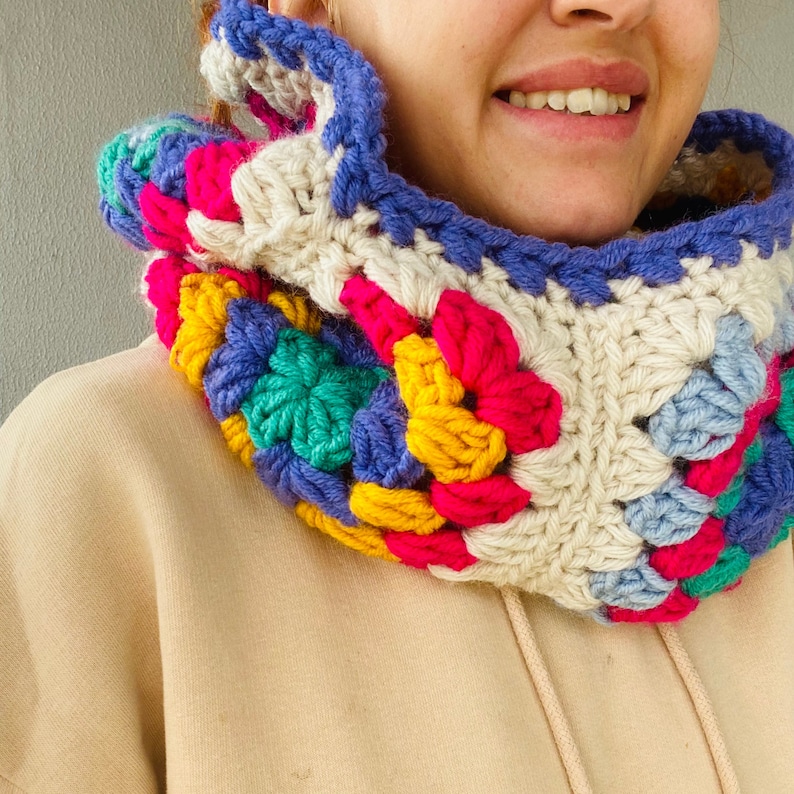 Puede incluir: Un cuello de ganchillo colorido con un patr&oacute;n de cuadrados de la abuela. El cuello presenta una mezcla de colores brillantes, incluyendo rosa, azul, amarillo, verde y crema. El cuello est&aacute; dise&ntilde;ado para ser usado alrededor del cuello y es un art&iacute;culo hecho a mano.