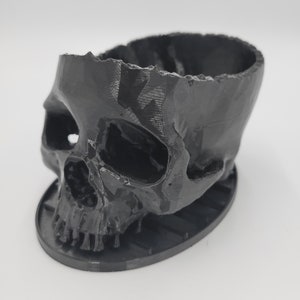 May include: Black skull-shaped planter with a smooth, matte finish. The planter has a round base and a hollowed-out skull design.