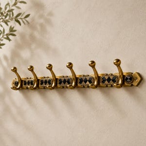 May include: A wall-mounted coat rack featuring six brass-toned metal hooks. The horizontal base is decorated with a repeating pattern of black and gold diamond-shaped inlays set within an antique-style metal frame with visible screw holes.